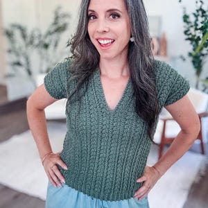 May include: A green crochet top with a v-neck and short sleeves. The top has a textured stitch pattern.