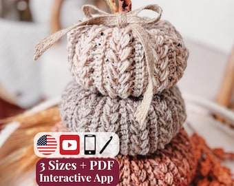 May include: A stack of three crocheted pumpkins in gradient shades of beige, taupe, and rust, topped with a small jute bow and a cinnamon stick stem. A white rectangular label displays the text 3 Sizes + PDF Interactive App with icons.