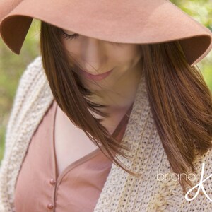 A woman wearing a cream crochet shawl wrap and hat, in a field of greenery.