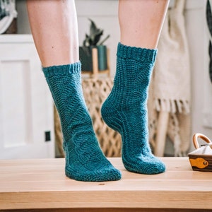 Puede incluir: Un par de calcetines de punto azul turquesa con un patrón texturizado. Los calcetines están sobre una superficie de madera.