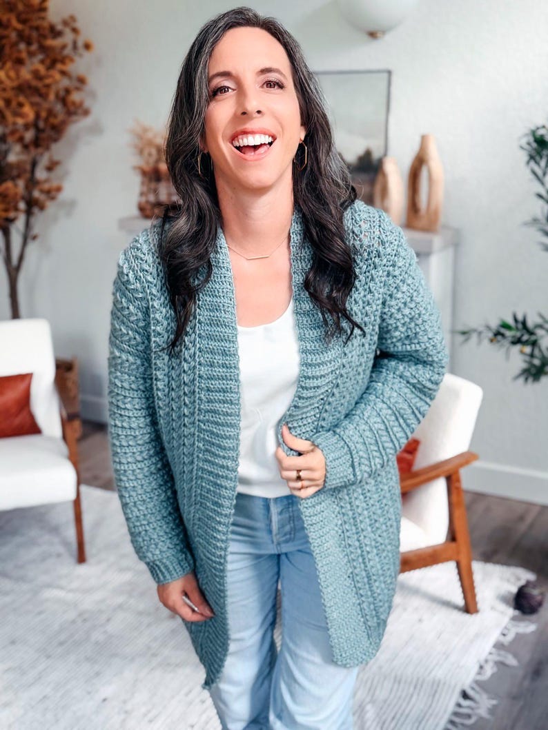 May include: A light blue crochet cardigan with a textured stitch pattern. The open-front cardigan is knee-length and worn over a white top and blue jeans. The cardigan has long sleeves and a relaxed fit, perfect for layering.