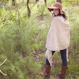 A woman wearing a cream crochet shawl wrap and hat, in a field of greenery.