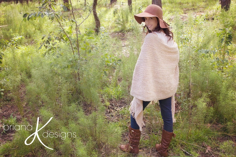 A woman wearing a cream crochet shawl wrap and hat, in a field of greenery.