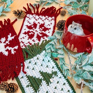 May include: Two crocheted scarves with a snowflake and reindeer design in red, white, and green. A small hamster is sitting in a red mug with a tree design.