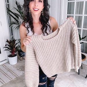 Woman smiling and holding up a beige crochet sweater.