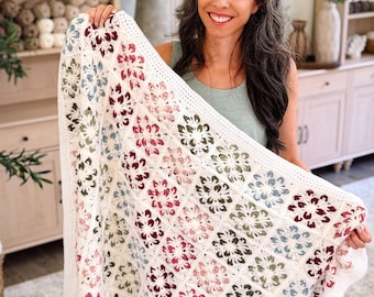 May include: A rectangular crochet blanket featuring a repeating floral motif pattern. The design consists of individual square blocks in cream, with flower centers in shades of deep red, sage green, and dusty blue, finished with a solid cream border.