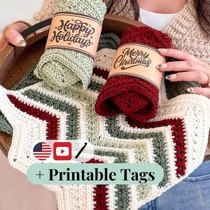 May include: Two crocheted washcloths in sage green and deep red, each wrapped in a tan paper band with black text reading Happy Holidays and Merry Christmas. Below them is a chevron-patterned crocheted cloth in cream, sage green, and deep red.