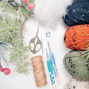 Crochet supplies flat lay with tweed yarn in navy, orange, green and cream, hooks, scissors, twine and stuffing