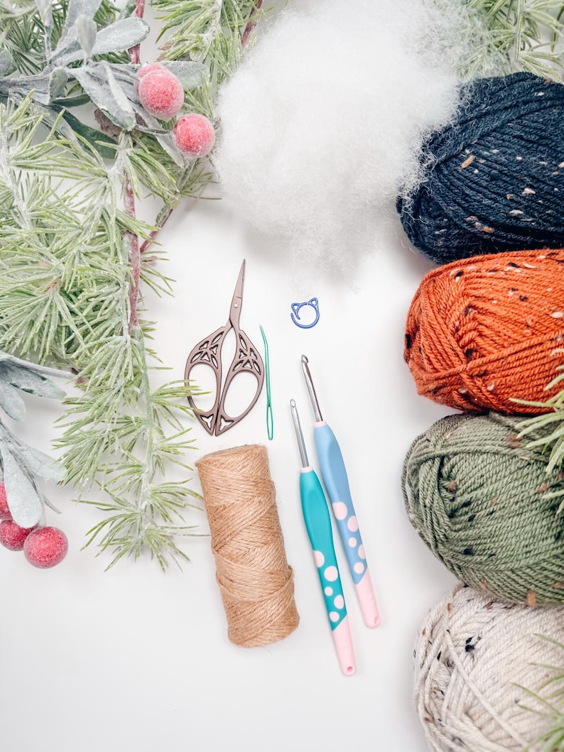 Crochet supplies flat lay with tweed yarn in navy, orange, green and cream, hooks, scissors, twine and stuffing