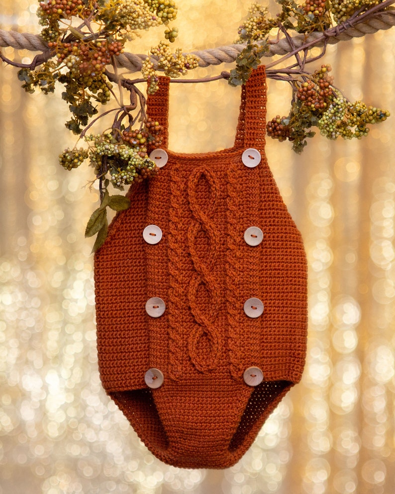 May include: A brown crocheted baby onesie with a cable knit pattern and wooden buttons.