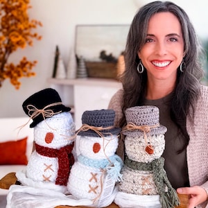Smiling woman holding a wooden tray with three crochet snowmen in red, blue and green scarves