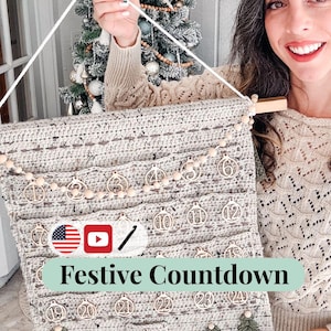 May include: A handmade, crocheted Christmas advent calendar in neutral tones. The calendar features wooden ornaments with numbers 1-25, wooden beads, and small green Christmas tree appliqués. The text "Festive Countdown" is displayed on the calendar.