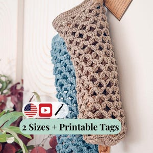 May include: Two crocheted produce saver bags, one beige and one blue, hanging against a white wall. The bags have a floral pattern and are tied with twine. A tag reads "2 Sizes + Printable Tags".