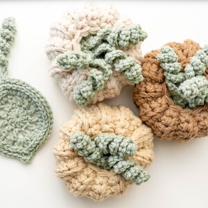 Three crochet pumpkins in cream, beige and tan with curly green stems next to a sage leaf coaster
