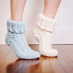 May include: A pair of crocheted slipper socks, one in light blue and one in white. The socks are folded down at the top and have a textured stitch pattern.