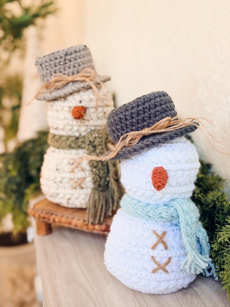 Wheat Stitch Snowman crochet pattern: two crochet snowmen on a shelf, one white with blue scarf and one speckled cream with green scarf, both in gray hats