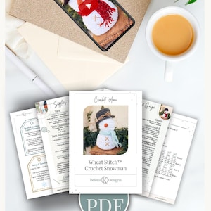 Pattern PDF pages and a phone showing the video tutorial for a crochet snowman beside a cup of tea