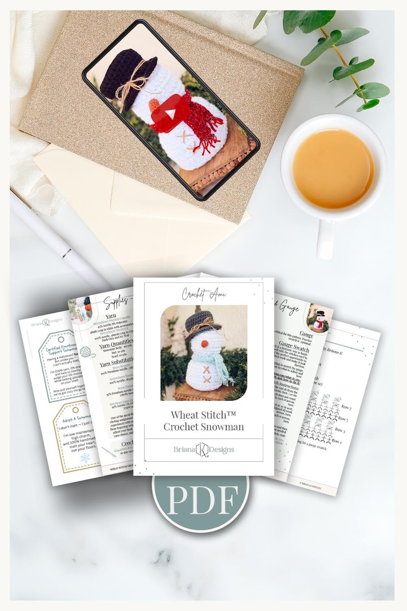 Pattern PDF pages and a phone showing the video tutorial for a crochet snowman beside a cup of tea