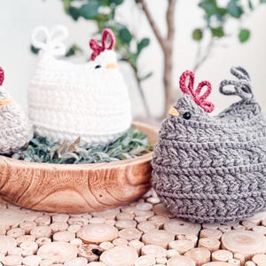 Gray, white, and oatmeal crochet chickens grouped around a wooden bowl on a wood slice tabletop