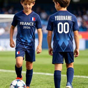 K&ouml;nnte beinhalten: Ein dunkelblaues Fu&szlig;balltrikot-Set bestehend aus Trikot und Shorts mit geometrischem Muster. Auf der Vorderseite steht FRANCE 2026 und eine franz&ouml;sische Flagge. Auf der R&uuml;ckseite ist der Text YOURNAME und die Nummer 00 in Wei&szlig; zu sehen.
