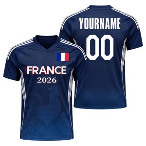 K&ouml;nnte beinhalten: Ein dunkelblaues Kurzarmtrikot mit V-Ausschnitt, wei&szlig;en Streifen an den Schultern und einer franz&ouml;sischen Flagge. Die Vorderseite zeigt den Text FRANCE 2026 mit einem Hahn-Motiv. Die R&uuml;ckseite zeigt den Text YOURNAME und die Nummer 00 in Wei&szlig;.