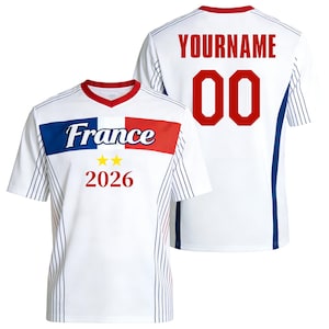 Op de afbeelding: Een wit shirt met korte mouwen, een rode kraag en blauwe en rode zijpanelen met dunne verticale strepen. De voorkant toont het woord France, twee gele sterren en het jaartal 2026. De achterkant toont de tekst YOURNAME en het nummer 00.