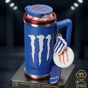 K&ouml;nnte beinhalten: Ein blauer 3D-gedruckter Dosenhalter mit Griff, der auf der Vorderseite das wei&szlig;e Monster Energy Logo zeigt. Der Halter verf&uuml;gt &uuml;ber einen blauen Deckel mit rotem Logo, einen roten Rand und eine Kugelkette mit drei Monster-Anh&auml;ngern.