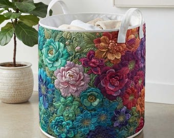 May include: A cylindrical fabric storage basket featuring a vibrant, multi-colored floral pattern with shades of teal, magenta, orange, and purple. The basket has two white fabric handles attached to the top rim and a white interior lining.