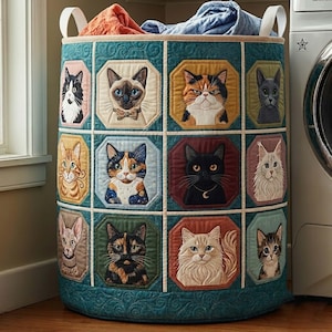 May include: A cylindrical fabric laundry hamper featuring a teal quilted exterior with a grid of twelve octagonal panels, each displaying a detailed embroidered portrait of a different cat breed. The hamper has two white handles and contains fabric.