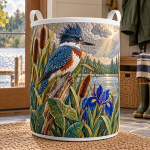 May include: A cylindrical fabric laundry hamper featuring a quilted design of a blue and white kingfisher perched on a wooden branch. The scene includes brown cattails, green foliage, a vibrant blue iris flower, and a lake landscape background.