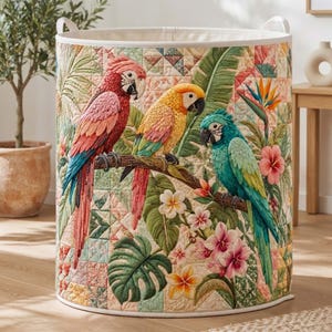 May include: A cylindrical fabric laundry hamper featuring a quilted patchwork design with a tropical theme. The exterior displays three colorful parrots in red, yellow, and teal perched on a branch, surrounded by green monstera leaves and flowers.