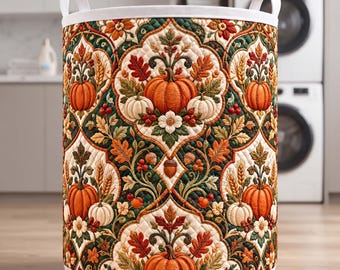 May include: A cylindrical laundry hamper featuring a quilted fabric exterior with a repeating pattern of orange pumpkins, white pumpkins, autumn leaves, acorns, and wheat stalks set against a dark green and cream background with white handles.