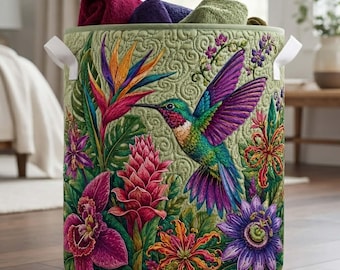 May include: A cylindrical fabric laundry hamper with a quilted light green background featuring a vibrant print of a hummingbird in flight surrounded by colorful tropical flowers including pink ginger, purple passion flowers, and orange bird of paradise.