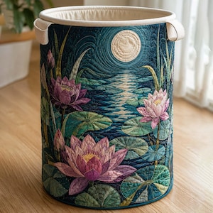 May include: A cylindrical fabric laundry hamper featuring a quilted exterior with a dark teal pond scene, pink lotus flowers, green lily pads, and a pale yellow full moon. The hamper has a cream-colored interior lining and two side handles.