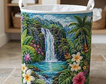 May include: A cylindrical fabric laundry hamper featuring a quilted exterior with a vibrant tropical landscape print. The design displays a cascading waterfall, lush green foliage, and colorful hibiscus and plumeria flowers.