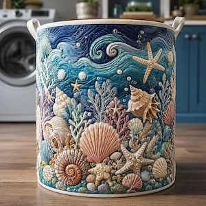 Könnte beinhalten: Ein zylindrischer Wäschekorb aus Stoff mit einem gesteppten Ozean-Motiv, das blaue Wellen, verschiedene beige und rosafarbene Muscheln, Korallenstrukturen und Seesterne zeigt, verziert mit kleinen weißen perlenartigen Akzenten.