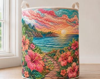 May include: A cylindrical fabric storage basket featuring a quilted tropical landscape scene. The design displays a stone path leading toward a beach, ocean, and sunset, framed by large pink hibiscus flowers and lush green foliage under a pink sky.