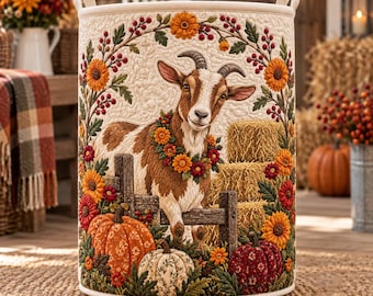 May include: A cylindrical fabric storage basket featuring a quilted design with a central brown and white goat wearing a floral wreath. The scene includes orange and red pumpkins, hay bales, and a wooden fence surrounded by autumn flowers.