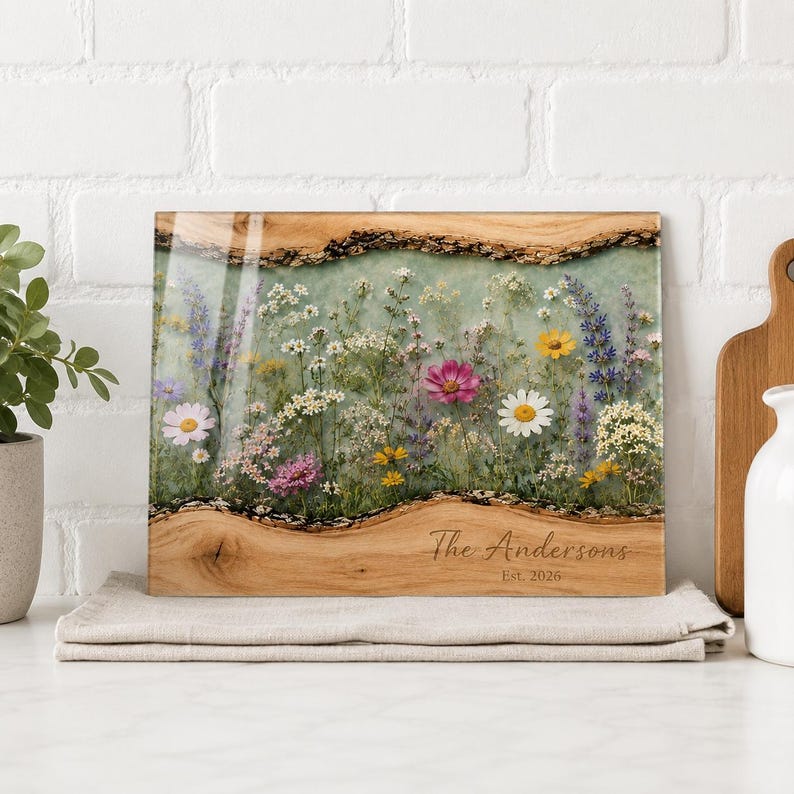 May include: A rectangular wooden serving board with live edges featuring a central resin inlay filled with pressed wildflowers in shades of pink, yellow, white, and purple. The wood is engraved with the text The Andersons Est. 2026.