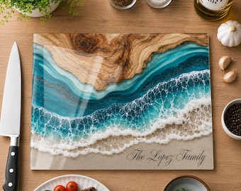 May include: A rectangular glass cutting board featuring a resin art design of a beach shoreline with wood grain, turquoise ocean waves, white sea foam, and sandy beach. The text "The Lopez Family" is printed in black script on the lower right corner.