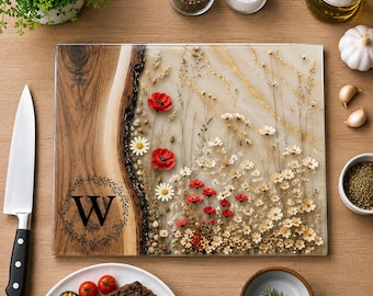 May include: A rectangular cutting board featuring a natural wood edge on the left side with a black letter W inside a circular wreath design. The right side is made of clear resin embedded with dried red poppies, white daisies, and tall grasses.