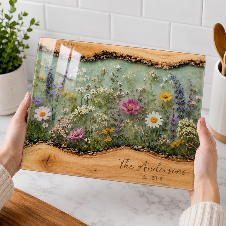 May include: A rectangular wooden serving board with a live edge and a central resin inlay featuring pressed wildflowers in shades of pink, yellow, white, and purple. The wood is engraved with the text The Andersons Est. 2026 in a script font.
