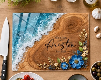 May include: A rectangular wooden serving board featuring a blue resin ocean wave design with white foam, decorated with blue and cream floral accents. The board is engraved with the text Mia & Tom Ariston Est. 2026 in a black script font.