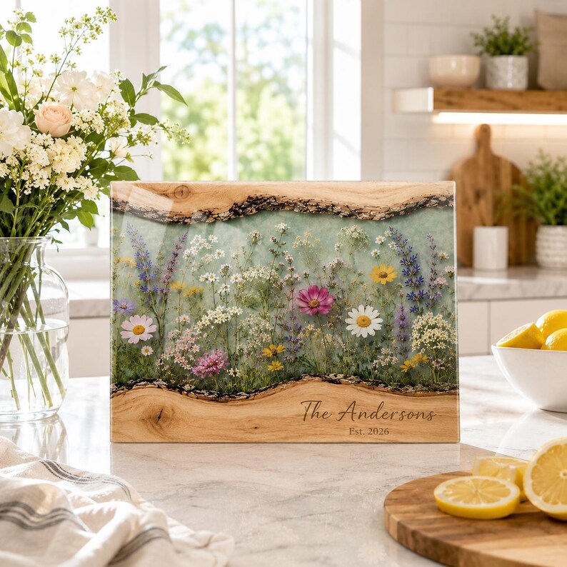 May include: A rectangular wooden serving board with live edges and a central resin inlay featuring a pressed wildflower meadow design. The board is engraved with the text The Andersons and Est. 2026 on the lower right wooden section.