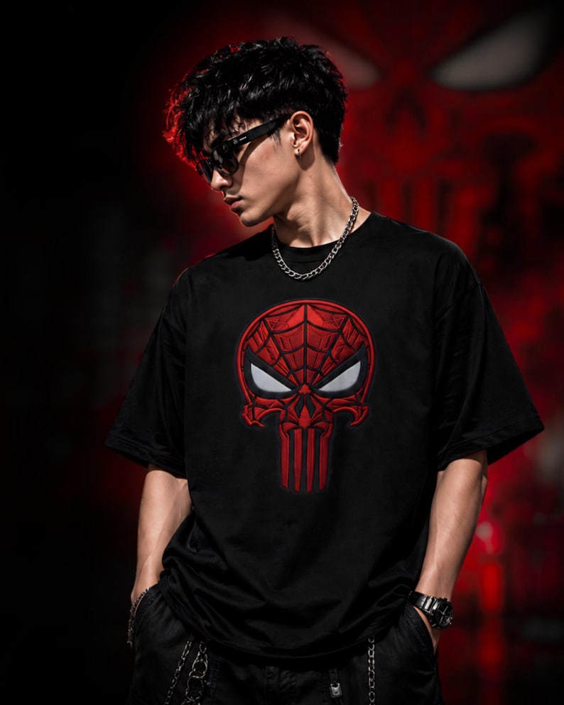 Pode incluir: Uma t-shirt preta de manga curta com um grande gr&aacute;fico bordado a vermelho no peito. O design combina um padr&atilde;o de teia de aranha na parte superior com uma forma de caveira por baixo, incluindo dois detalhes oculares brancos em am&ecirc;ndoa.