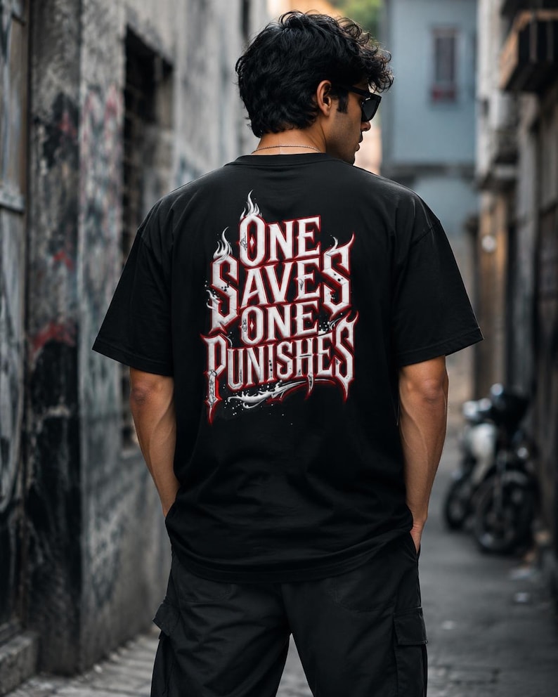 Pode incluir: Uma t-shirt preta de manga curta com um gr&aacute;fico nas costas apresentando o texto branco e vermelho "ONE SAVES ONE PUNISHES" numa fonte g&oacute;tica estilizada, acentuado com detalhes de chamas e um elemento gr&aacute;fico afiado na parte inferior.