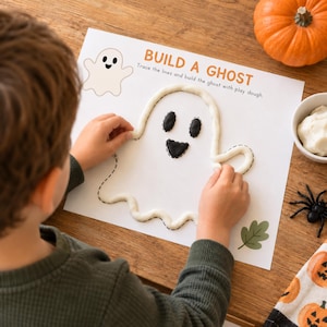 Peut inclure: Une feuille d'activité en papier blanc intitulée BUILD A GHOST avec des instructions pour tracer des lignes et construire un fantôme avec de la pâte à modeler. La feuille présente un contour de fantôme en pointillés partiellement rempli.