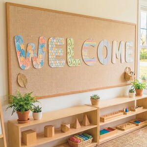 May include: A large rectangular cork notice board with a light wood frame displays the word WELCOME in colourful, patterned cutout letters. Below, two light wood shelves hold various wooden geometric shapes, small potted plants, and a basket.