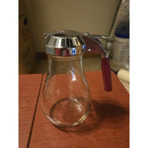 Dispensador de jarabe de vidrio con diseño de goteo estilo vintage, mango rojo, tapa cromada, menaje de cocina retro.