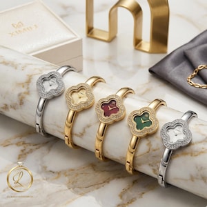 Puede incluir: Cinco relojes tipo brazalete con esferas en forma de trébol y biseles con cristales incrustados. Los relojes tienen correas en tonos plata y oro con esferas blancas, doradas, rojas y verdes. Cada esfera muestra el nombre de la marca XIMILI.
